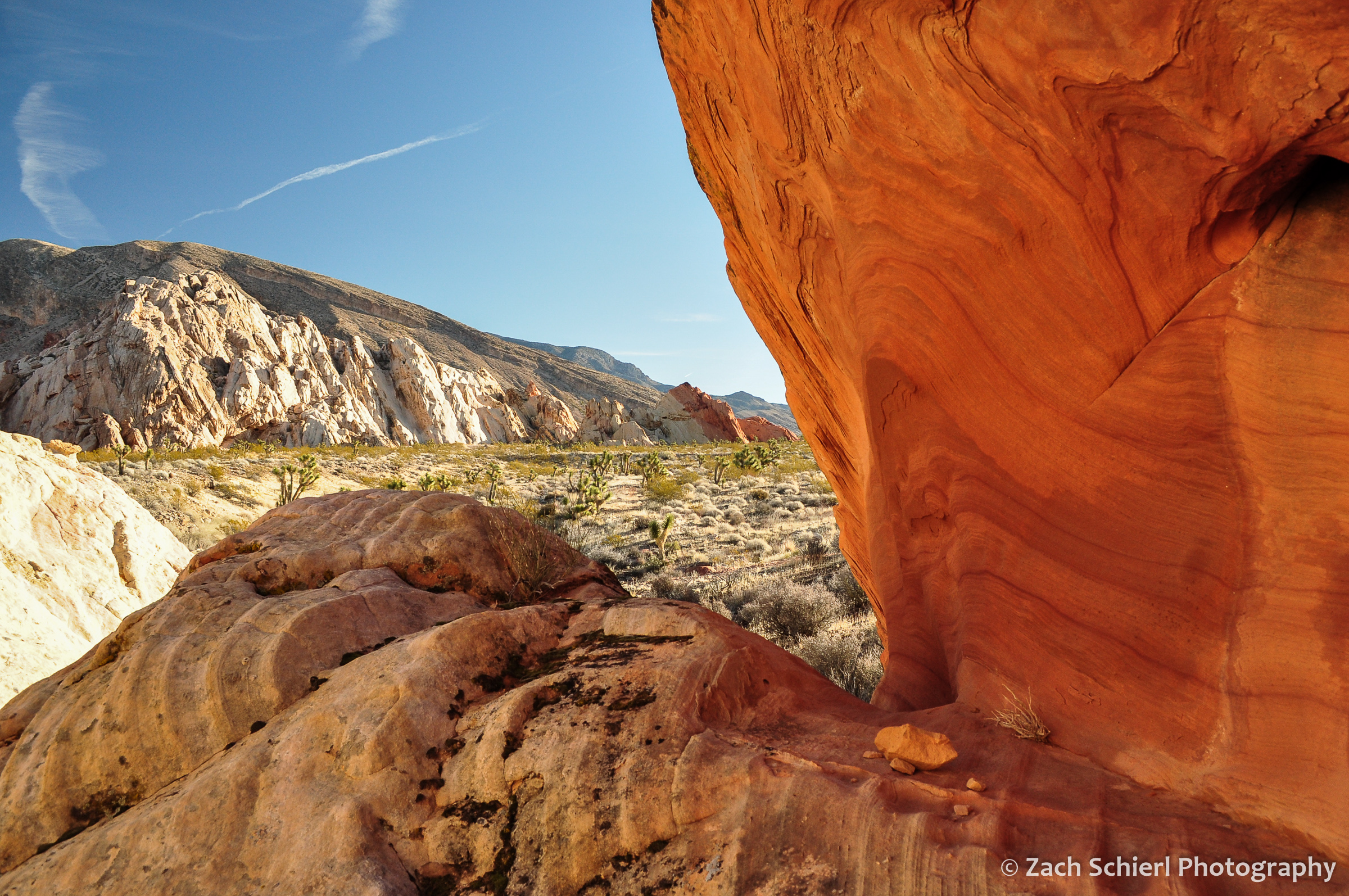 A notch in a sandstone boulder frames a view of a desert landscape.