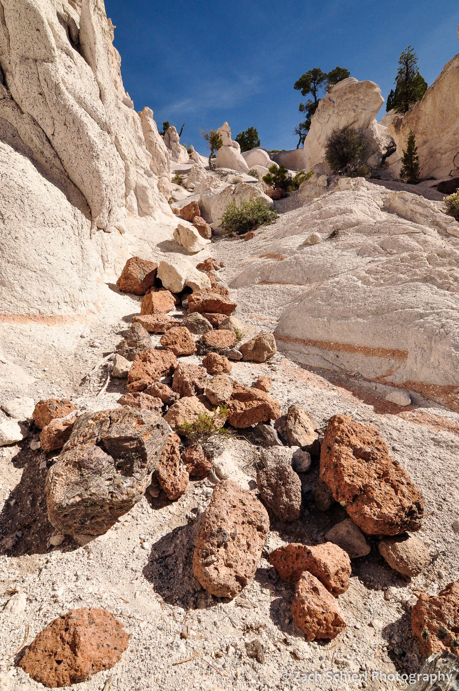 Pink and brown boulders lie strewn in a chute of white tuff