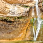 A large waterfall dwarfs a hiker approaching for a photo.