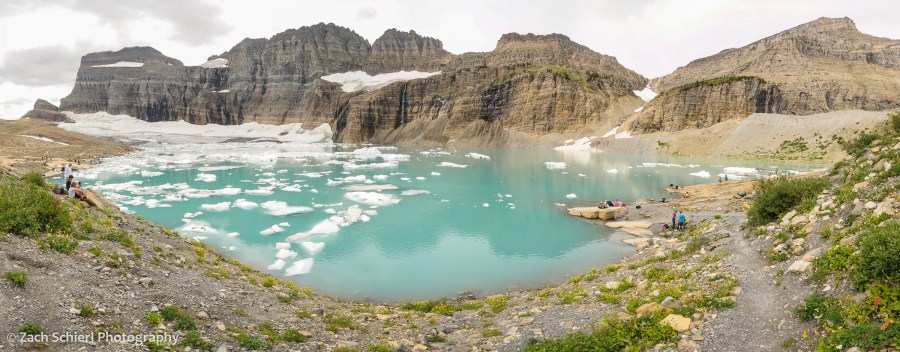 Cliffs of rock surround several glaciers and an azure-blue lake containing numerous icebergs. 