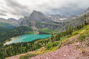 Dark clouds loom over a range of mountains and an azure-blue alpine lake