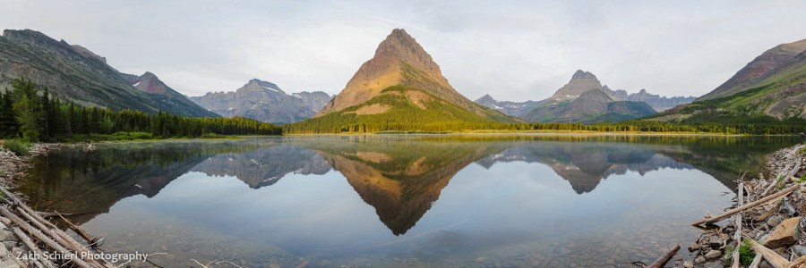 A series of sharp mountain peaks are reflected in a tranquil lake at sunrise. 
