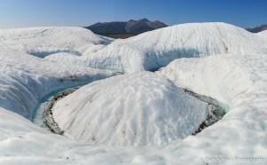 A channel of water flowing across a white glacier carves a tight bend in the ice