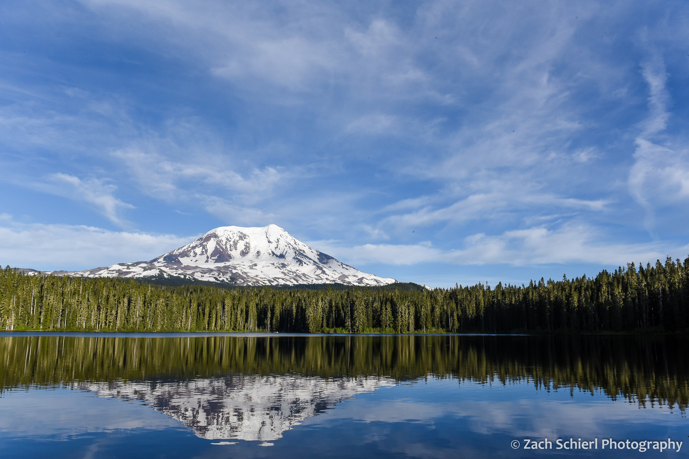 Volcanic cone and wispy clouds reflected in a tranquil mountain lake.