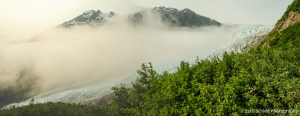 A valley containing a glacier is partially obscure by a bank of clouds