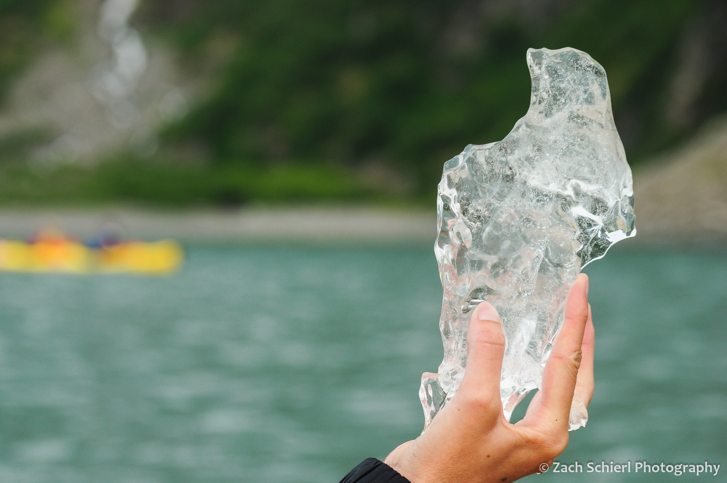 A hand holds a small piece of ice that has broken off of a glacier