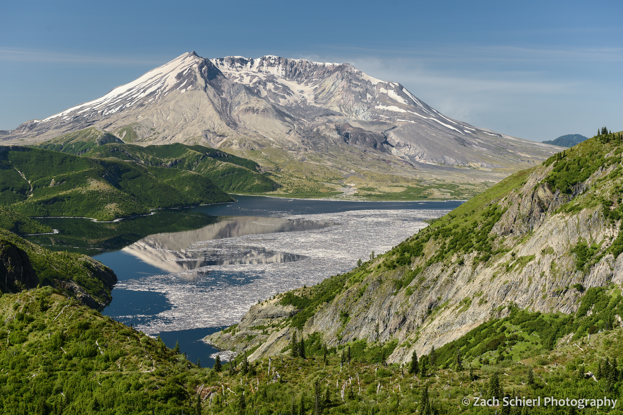 A volcanic cone rises behind a lake covered with floating logs