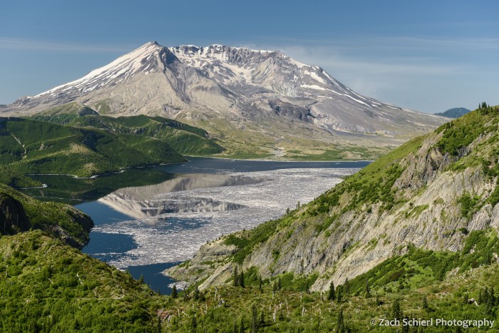 A volcanic cone rises behind a lake covered with floating logs