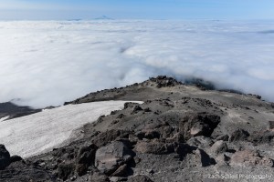 Dark, jagged volcanic rocks on the slopes of Mt. St. Helens with clouds far below