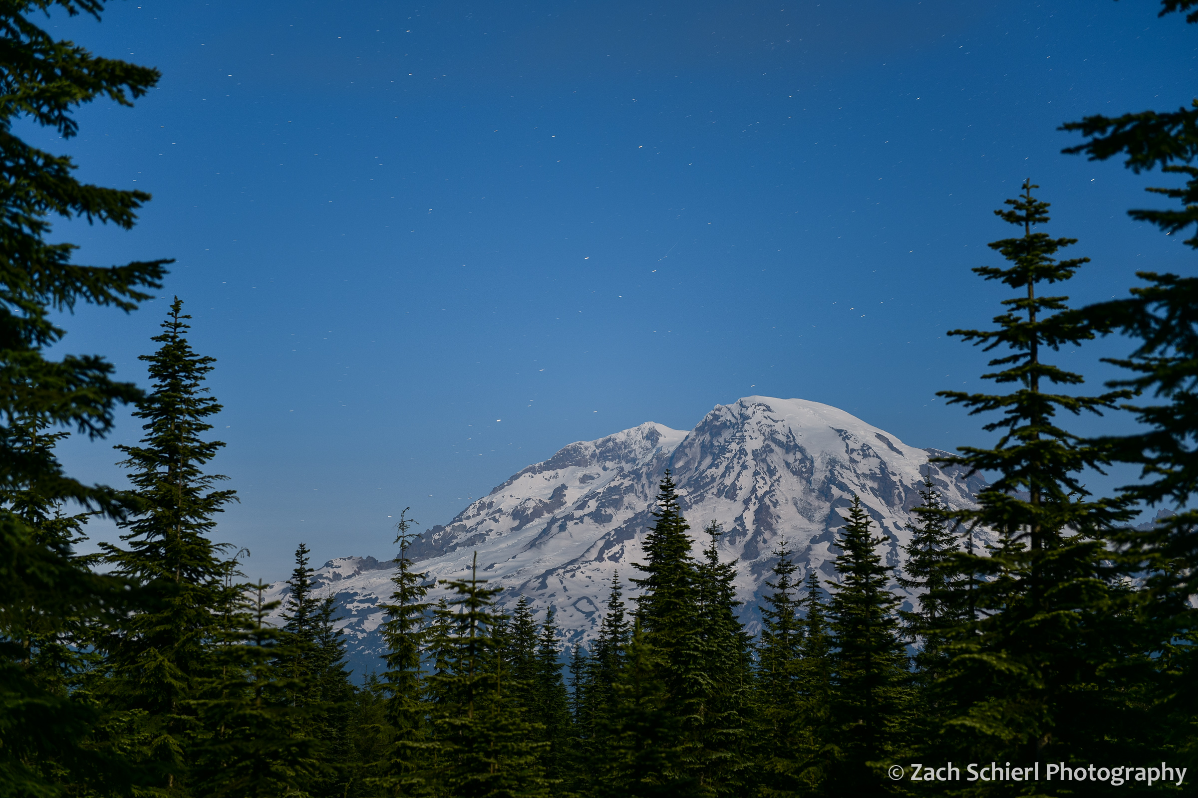 A large volcanic peak illuminated by moonlight with stars in the background sky.