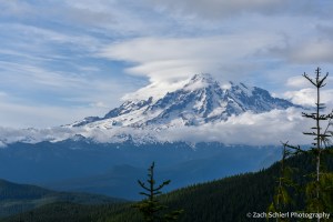 A series of stacked lenticular clouds above a conical volcanic peak