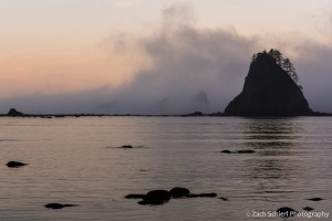Clouds and mist surround several large rocky islands sitting in a calm bay