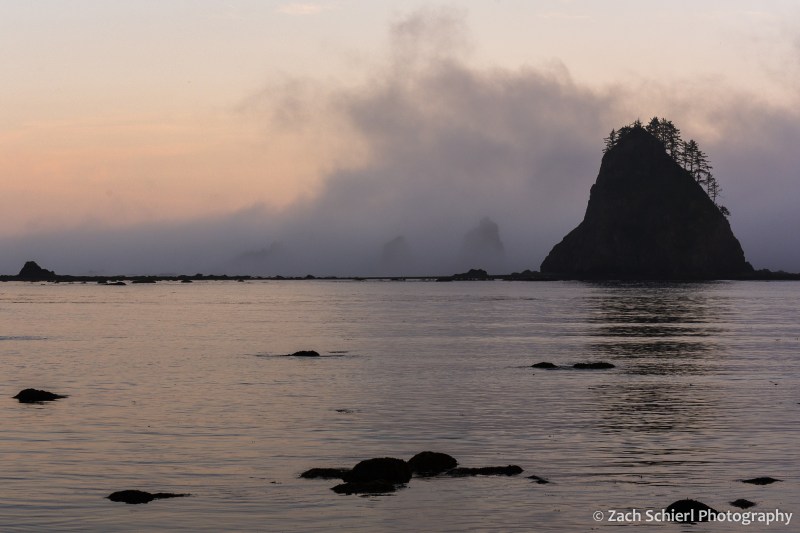 Clouds and mist surround several large rocky islands sitting in a calm bay