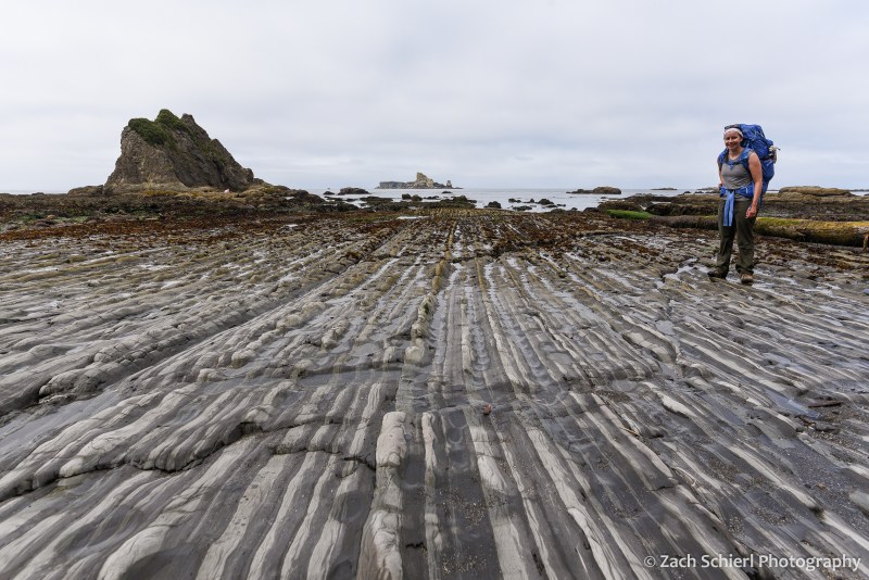 Alternating bands of dark and light colored rock stretch to the horizon along the coastline.