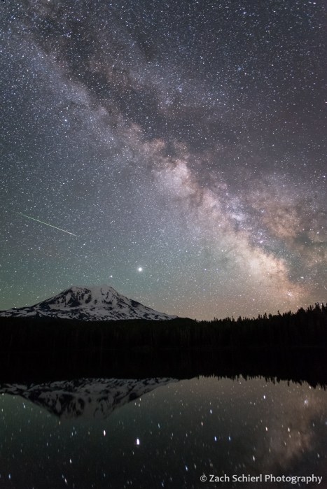A photograph of the Milky Way galaxy hovering over a tall volcanic peak.