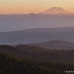 The sky is filled with pink, orange, and purple as the sun sets on a forested scene