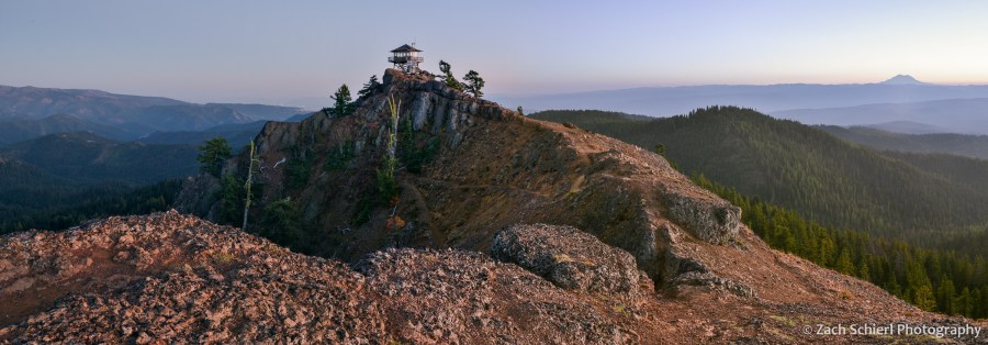 A rocky ridge with a lookout tower on top is seen as the sky darkens to twilight in the background