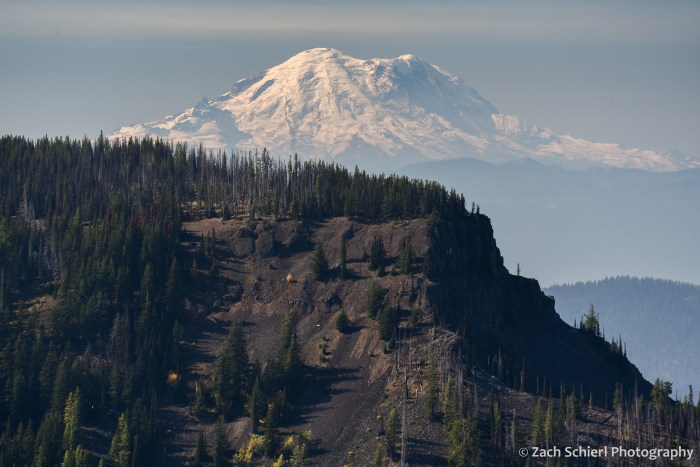 A tall snowy peak rises above dark volcanic cliffs in the foreground