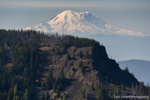 A tall snowy peak rises above dark volcanic cliffs in the foreground
