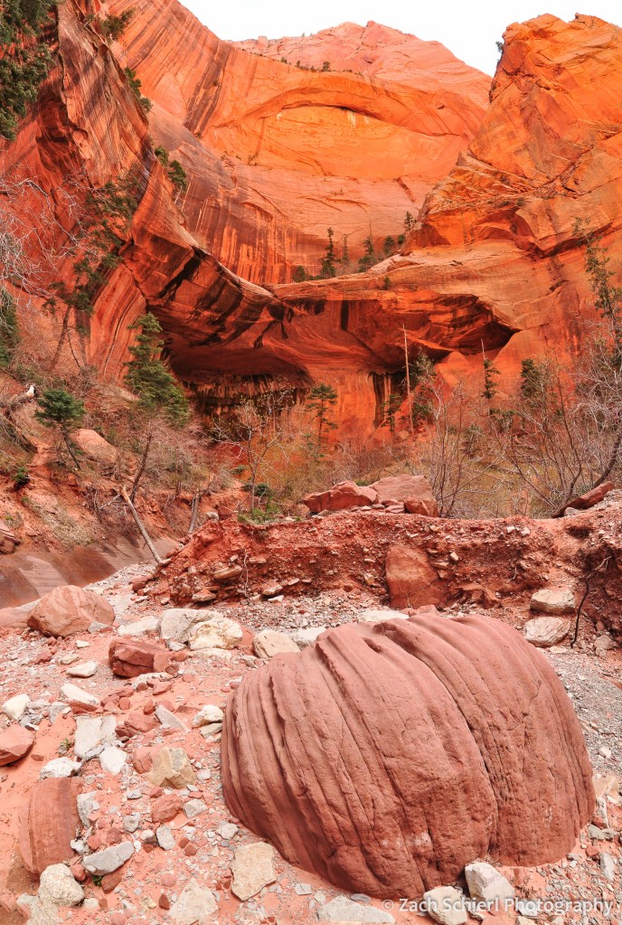 White and red boulders sit in a dry wash with towering orange cliffs above
