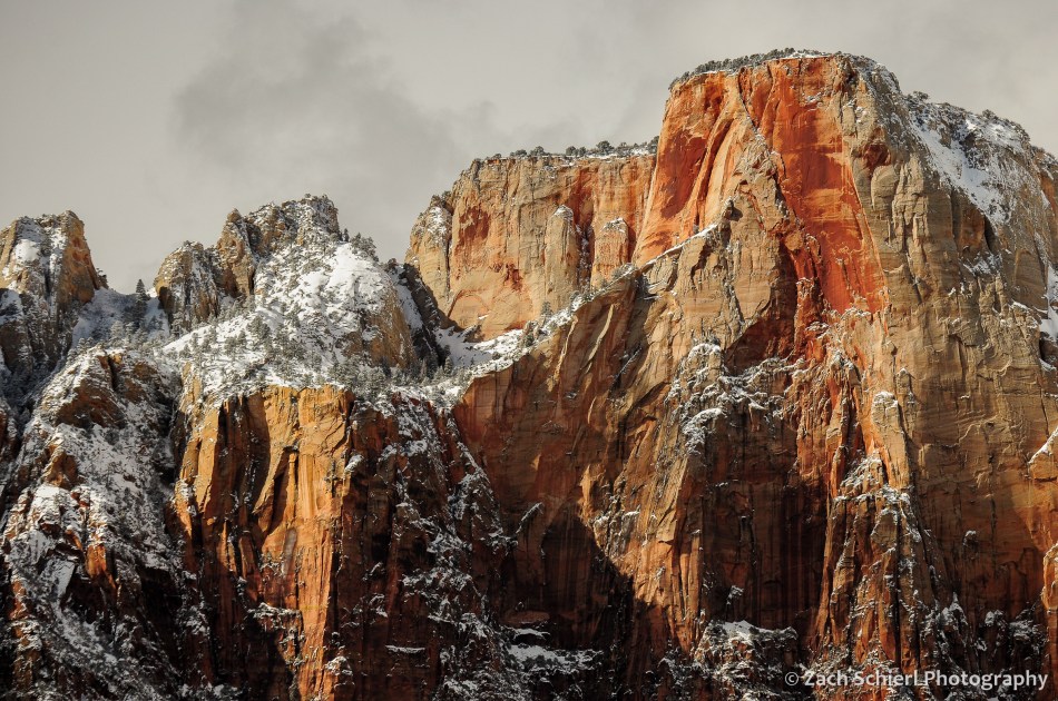 Cliffs of white and tan rock are streaked by dark red coloring, and dusted by a light layer of white snow.