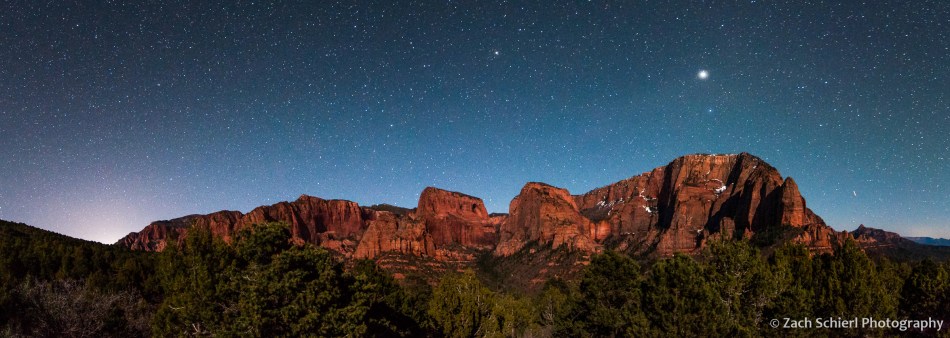 Stars and planets dot the sky over cliffs and canyons of red rock