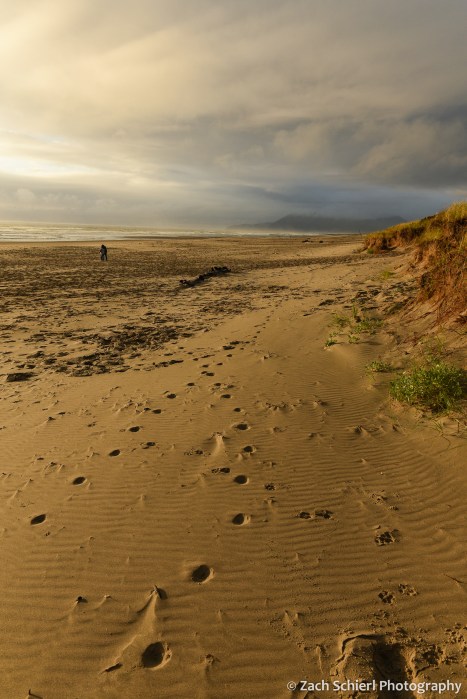 A sandy beach covered in footprints extends toward a horizon filled with dark clouds