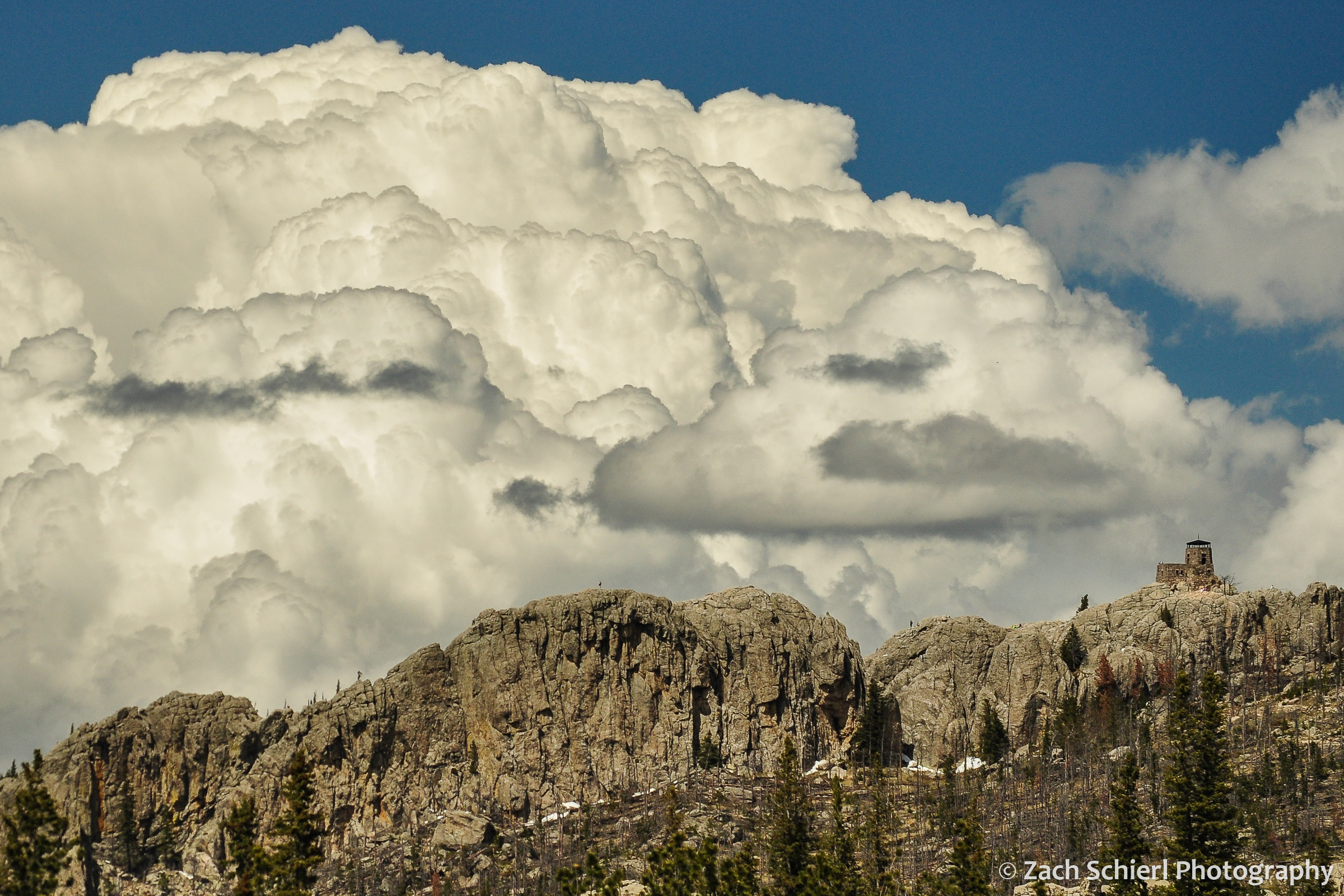Towering white clouds hover over a rocky ridge with a small lookout tower