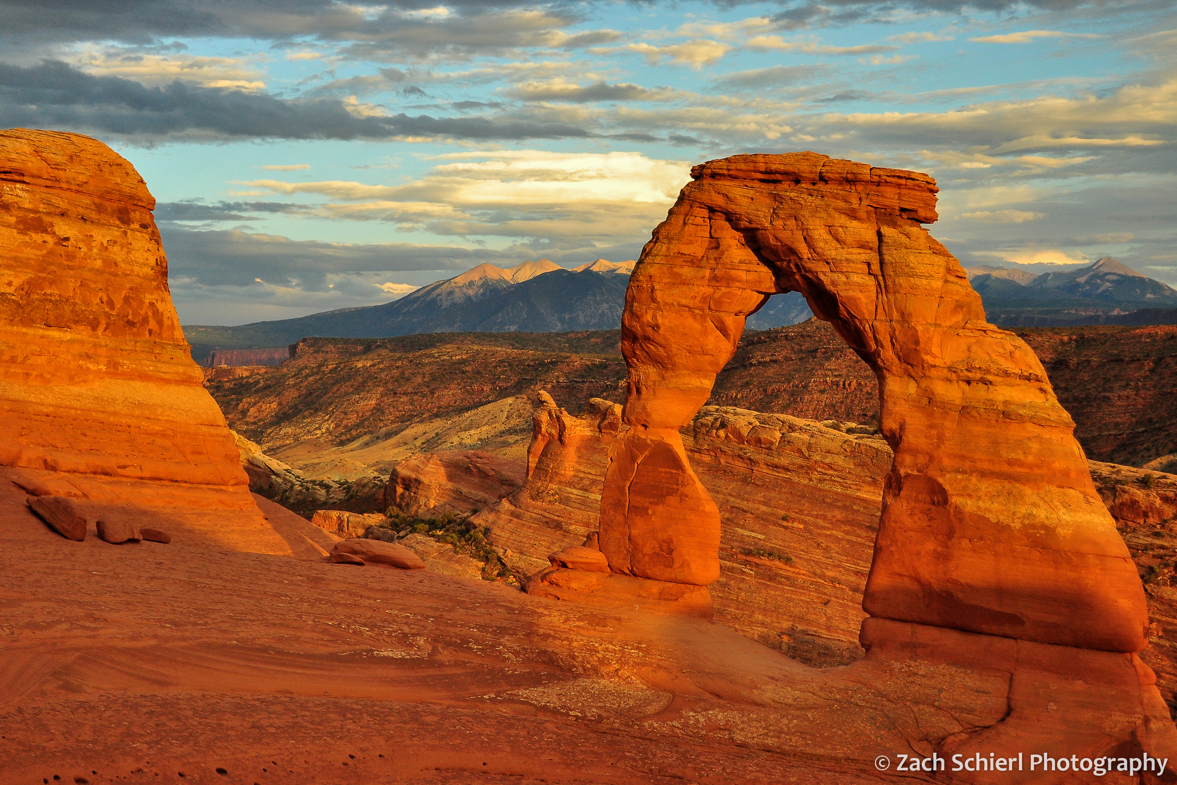 An orange sandstone arch frames a distant mountain range at sunset