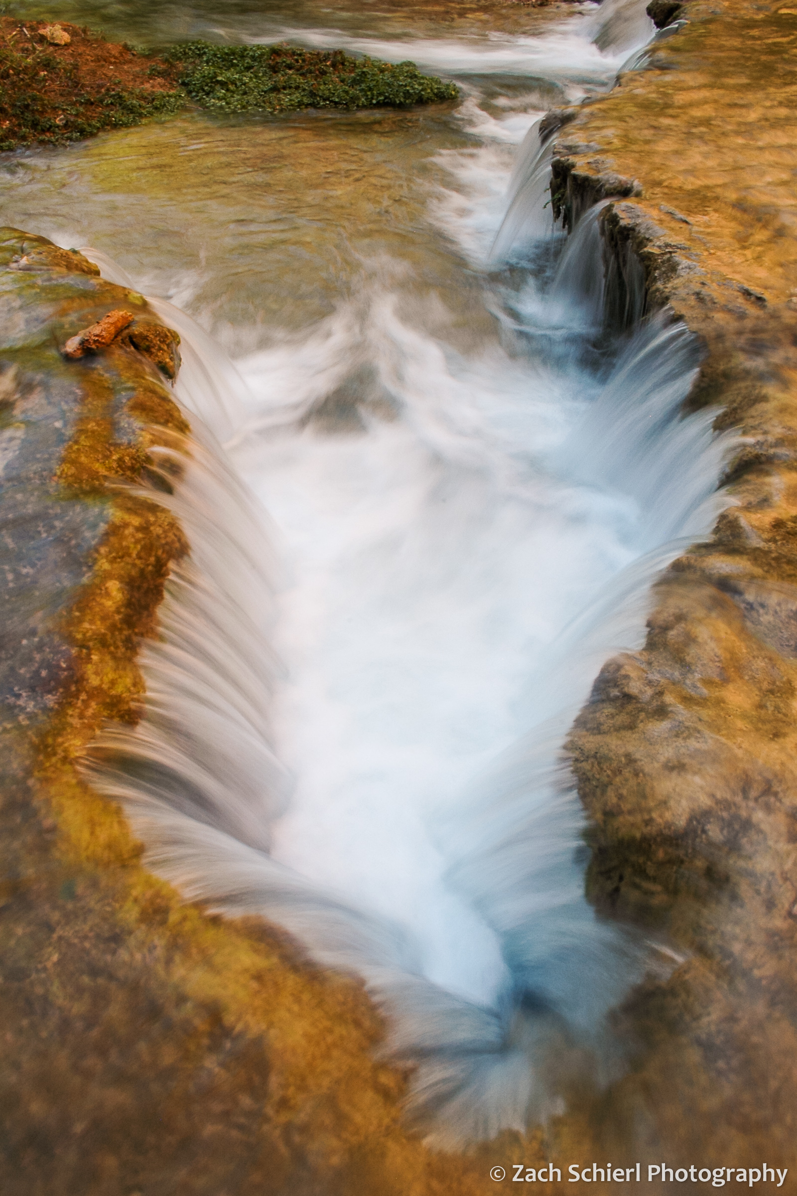A small waterfall cascades over orange and brown rocks
