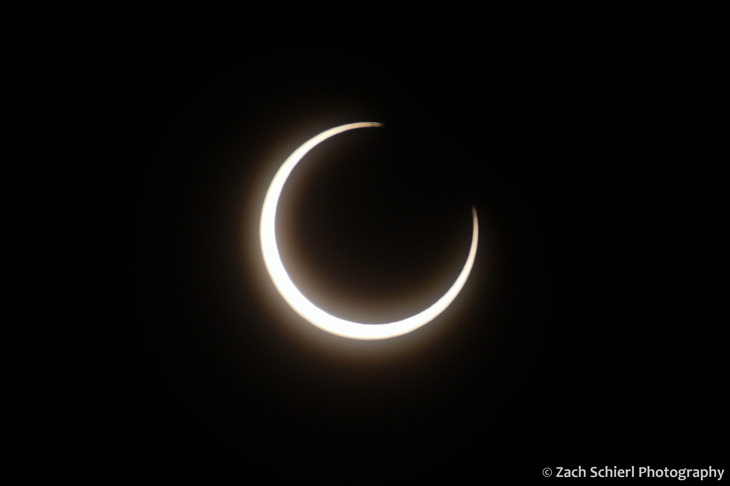 A broken ring of sunlight nearly surrounds the dark moon