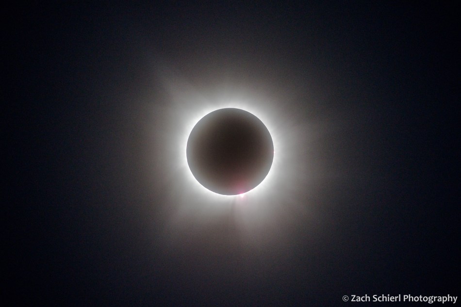 Faint streamers of light extend away from the dark new moon during a solar eclipse
